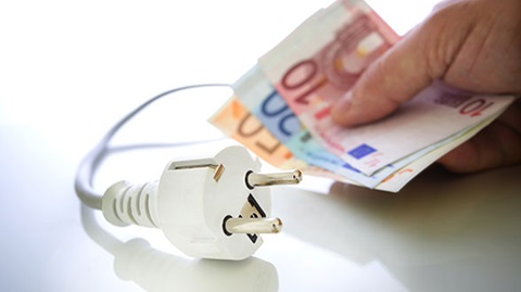 main tenant une liasse de billets devant une prise électrique